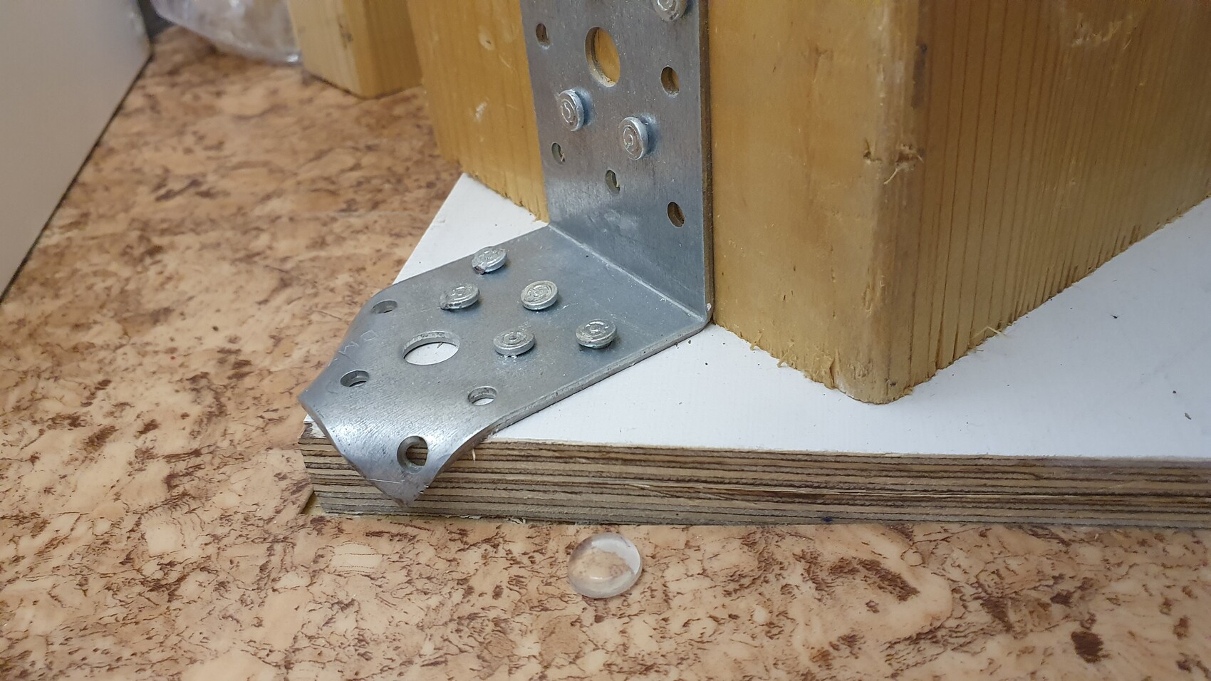 Metal bracket reinforcement on wooden post, visible screws, wooden base plate.