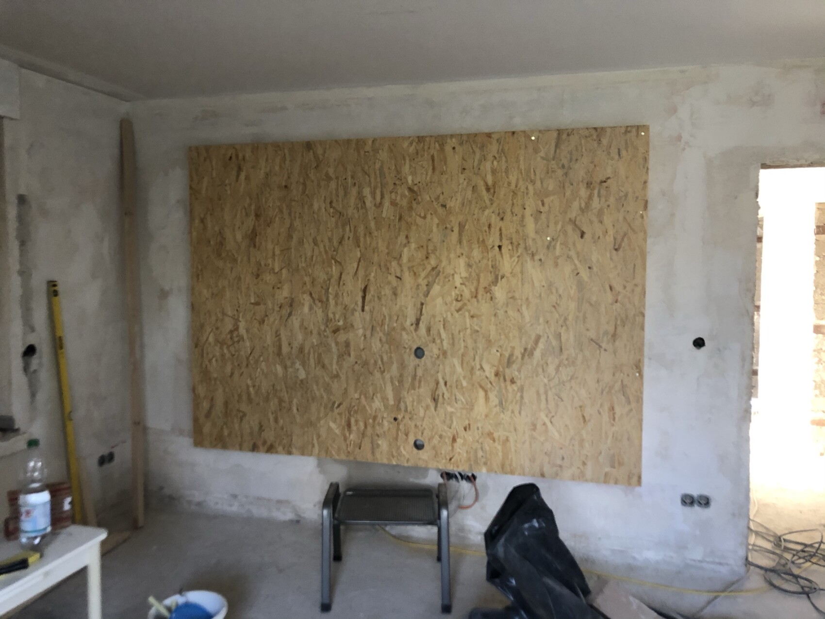 Renovierungsraum mit OSB-Platte an der Wand, Werkzeugen, Kabeln und hellem Durchgang.