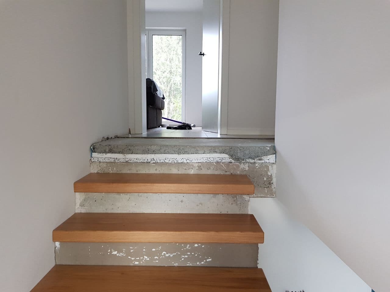 Wooden staircase with concrete substructure, open door area to the hallway and view outside.