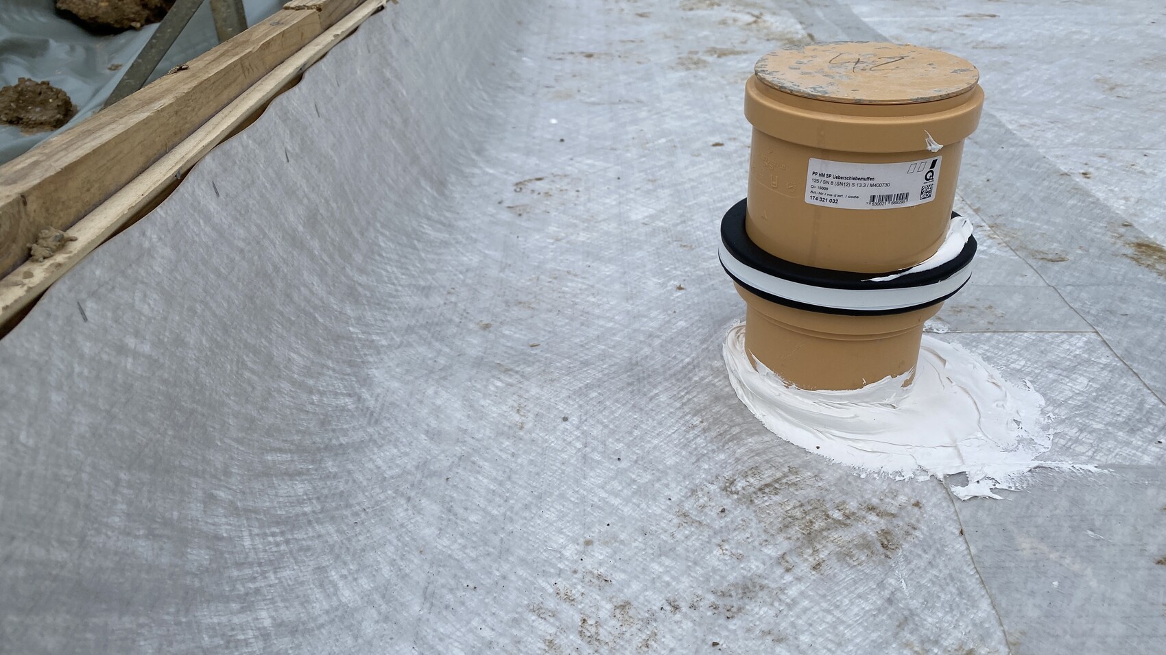 Brown roof vent/pipe penetration sealed with white sealing compound on the roof membrane, wooden battens on the left.