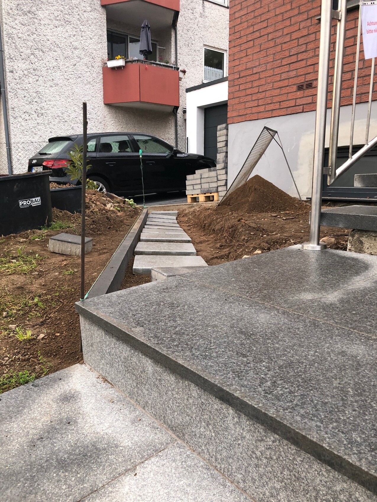 Construction site in front of residential house: Stone steps lead to entrance; pile of gravel, pallets, black car.