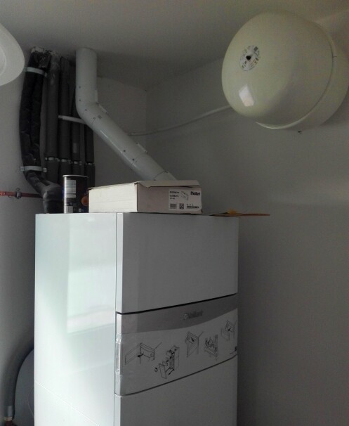 Weißer Heizkessel mit Rohren, Dehnungsgefäß an der Decke, Karton darauf.