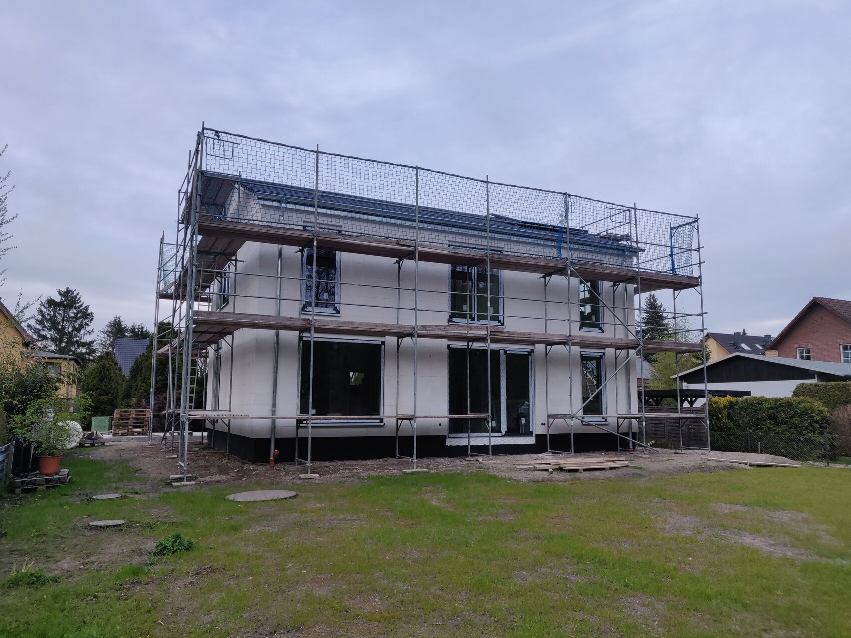 Two-story house with white facade, surrounded by scaffolding; construction work in the garden.