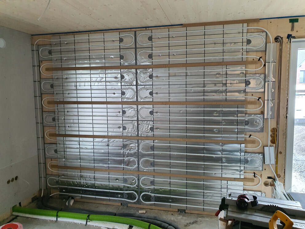 Unterbau einer Fußbodenheizung: Mehrere Rohrschlangen in Metallplatten auf Holzrahmen montiert.