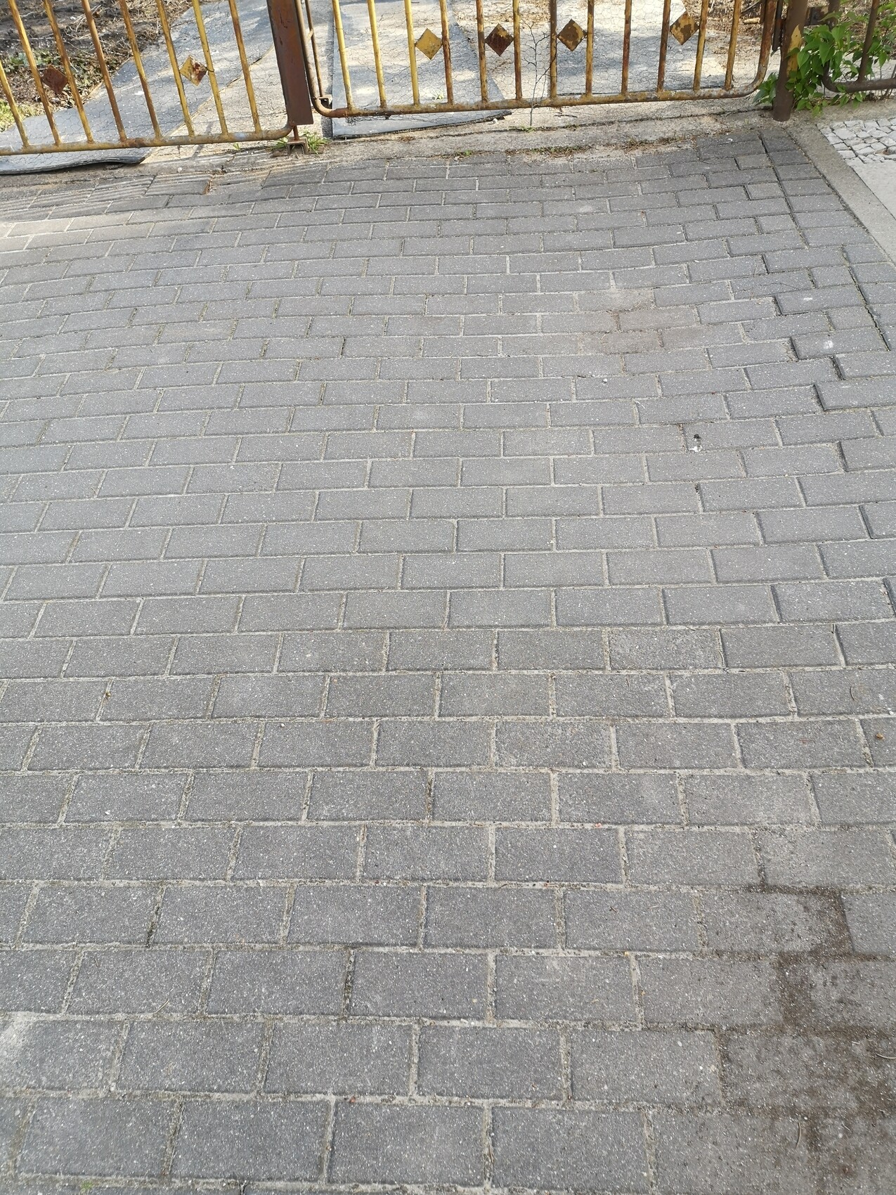Paved forecourt made of gray paving stones in front of a metal gate
