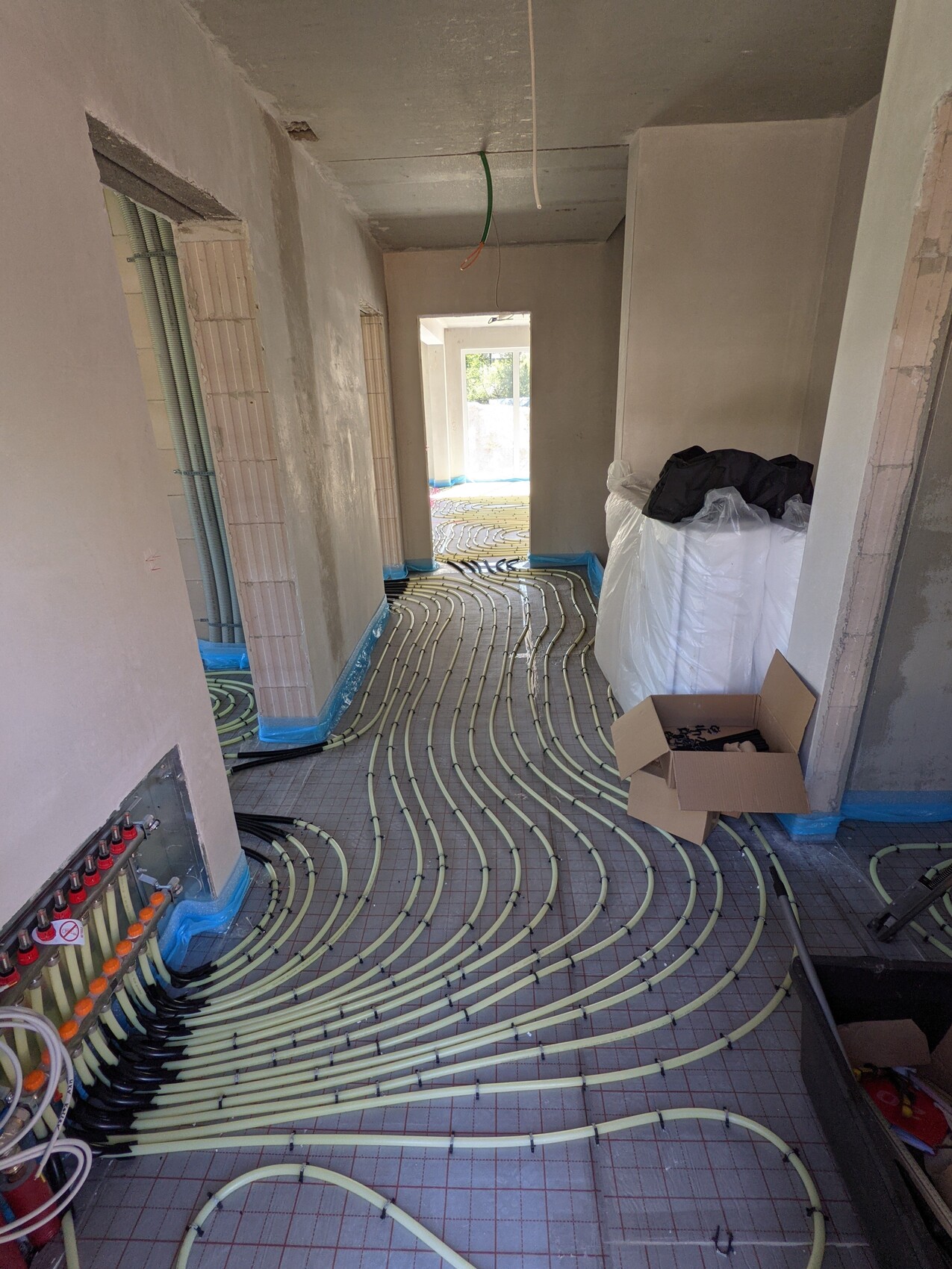 Bau-Raum mit verlegten Fußbodenheizungsrohren, Verteiler links, Karton mit Bauteilen