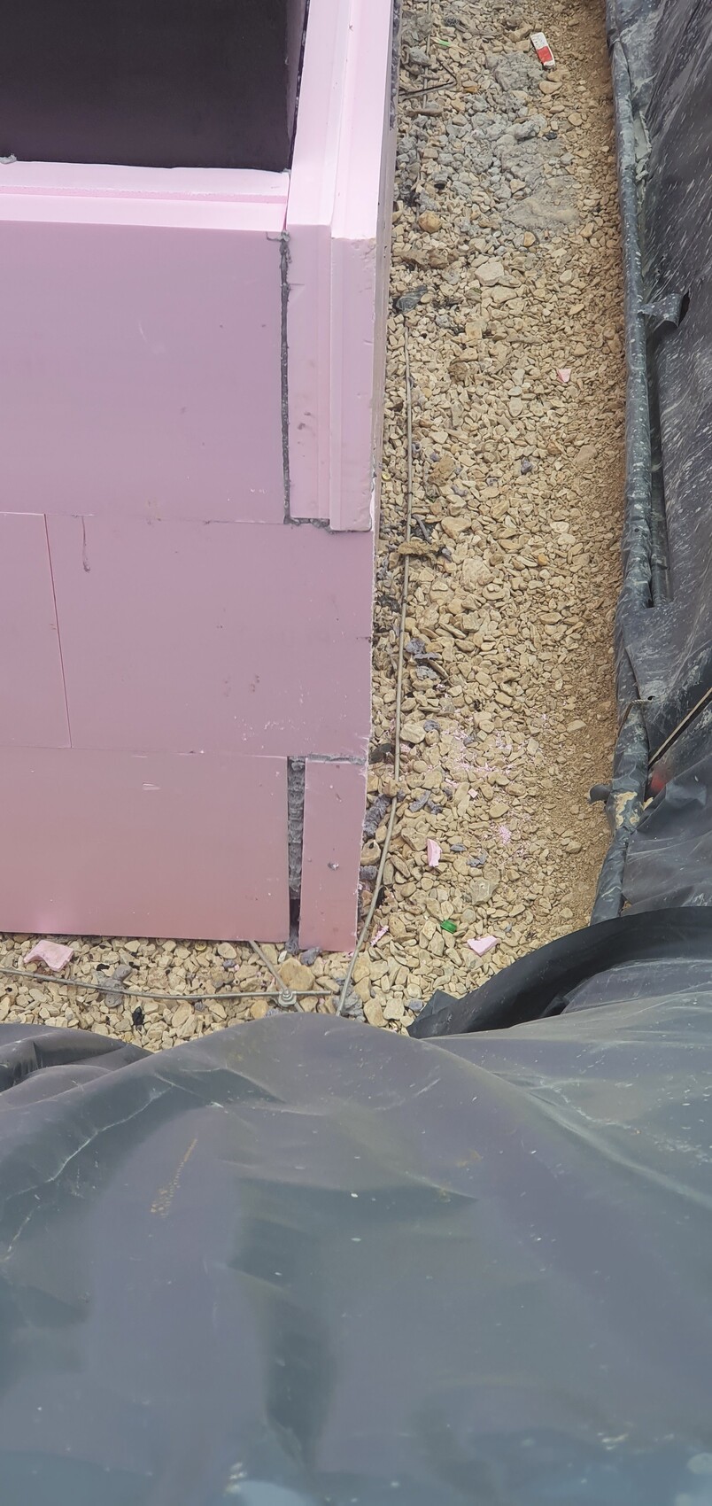 Construction site with pink insulation panels on a wall, gravel floor and black construction tarp.