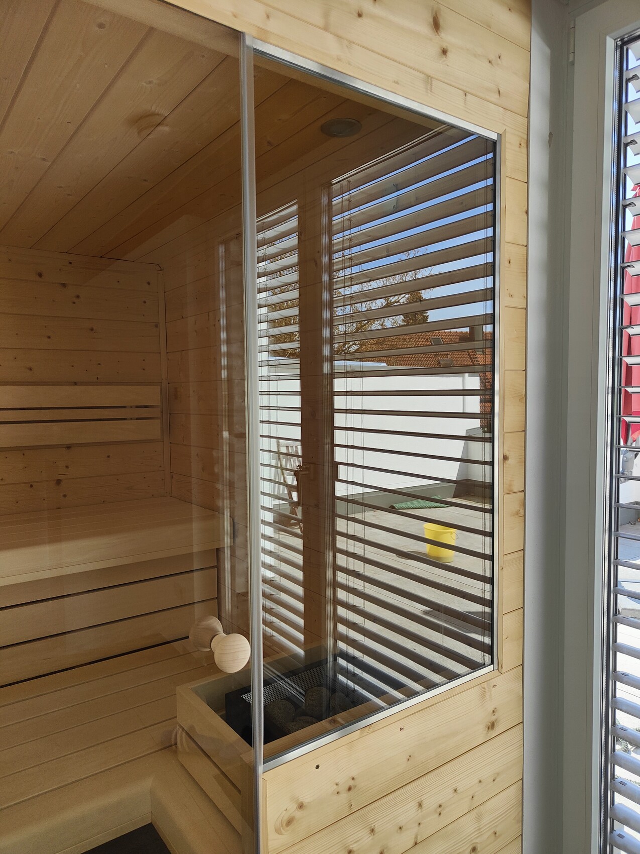Wooden sauna with glass wall, interior bench, and wood paneling; exterior slatted window.
