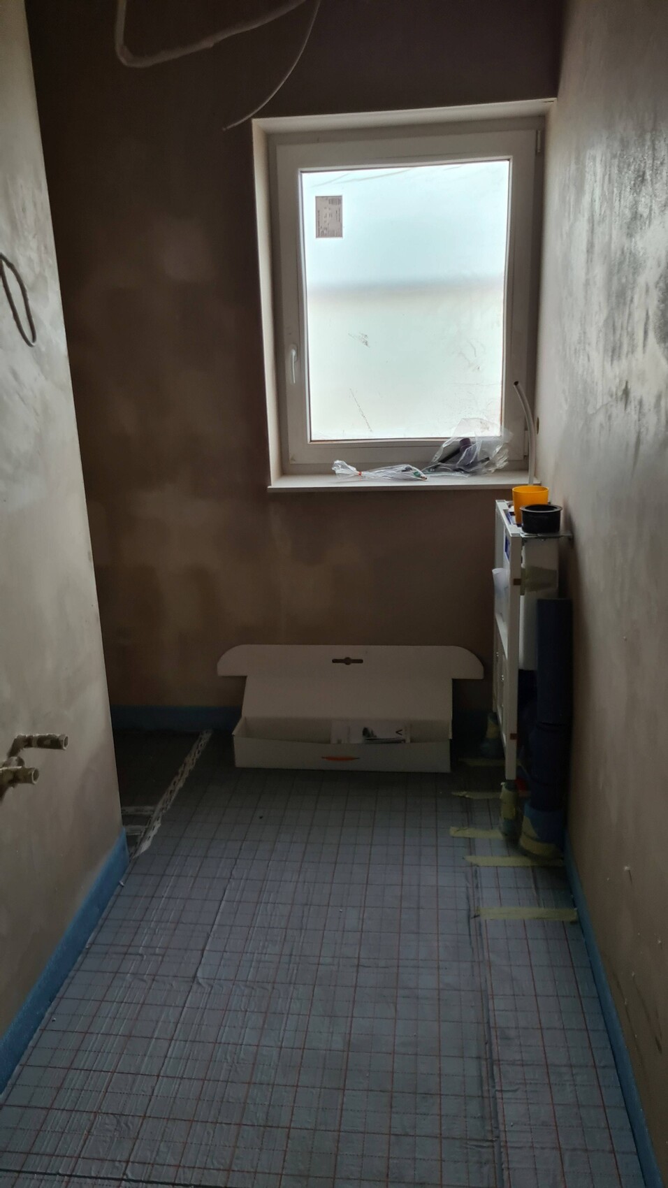 Small bathroom under construction with window, cardboard box, and shelf full of containers.