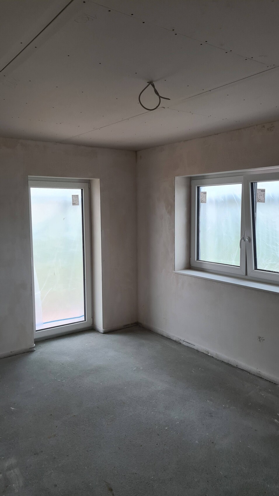 Room under construction with two windows, door window; unfinished walls, cables in the ceiling.