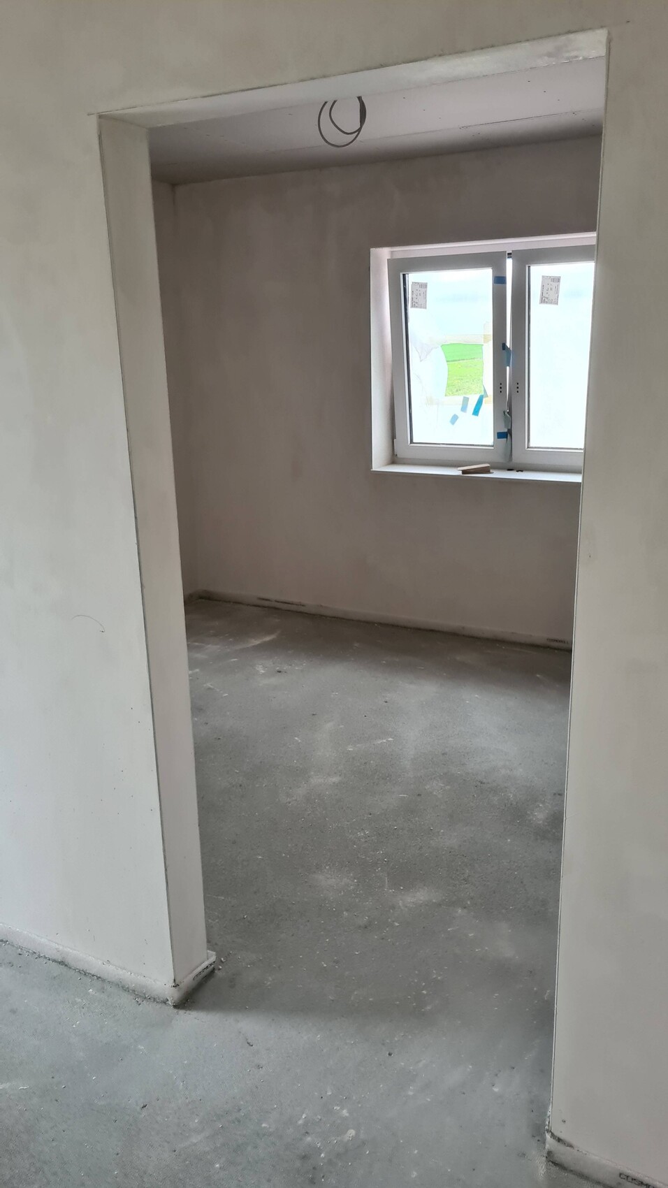 Unfurnished room under construction with raw walls, concrete floor, and window.