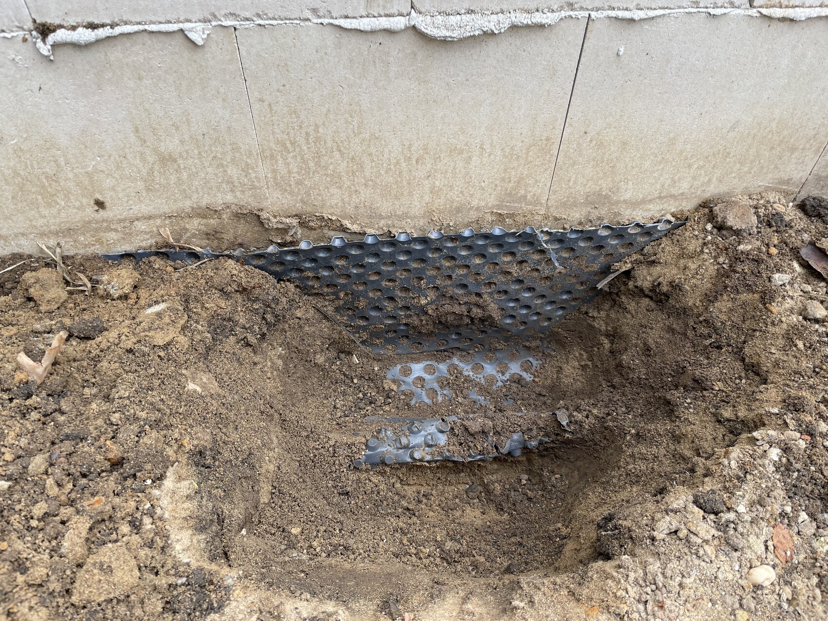 Trench next to the house foundation; blue perforated drainage panel in the soil.