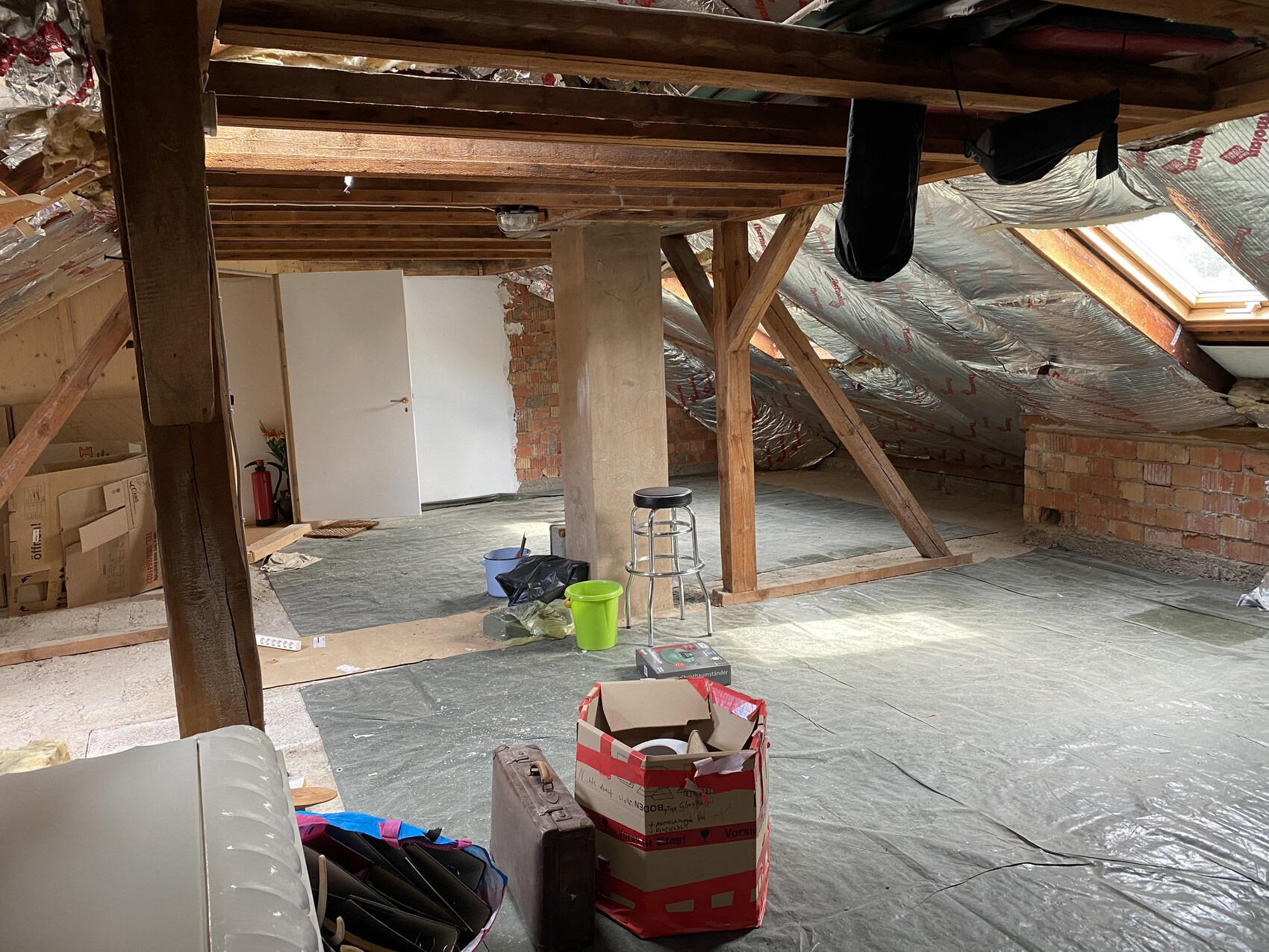Attic under renovation: beams, insulation, foil on the floor, white door in the background.