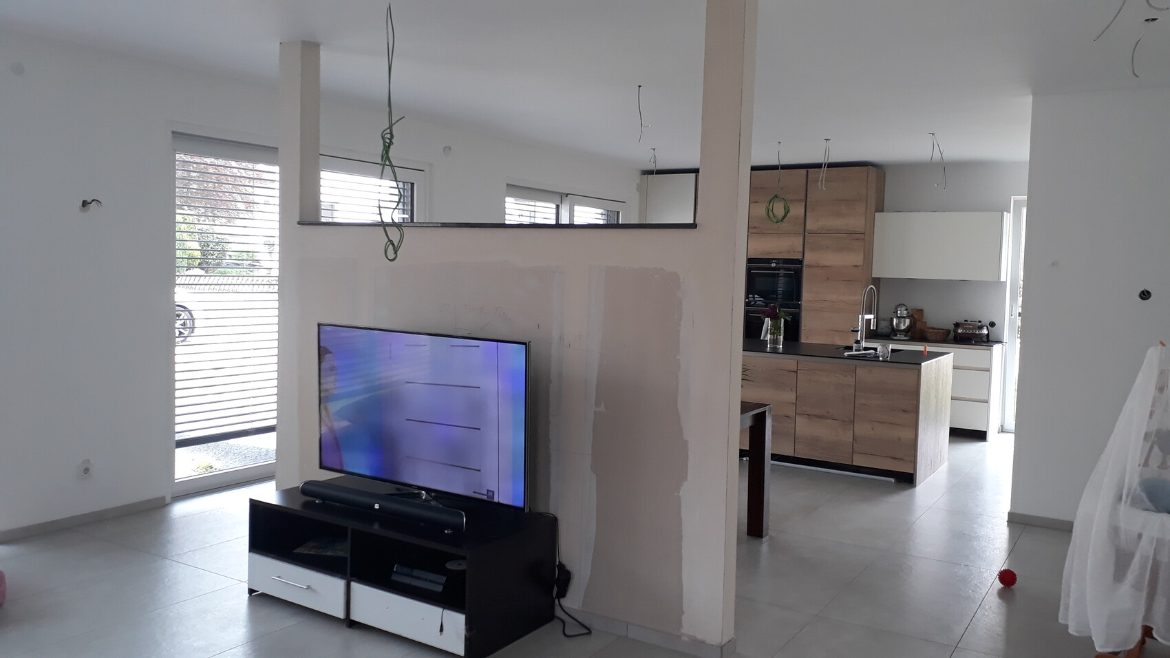 Open living room with TV on TV stand, kitchen island, visible cables, and unfinished wall.