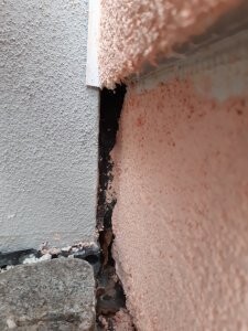 Close-up of cracking in the wall at the joint between building components, crumbling plaster visible.