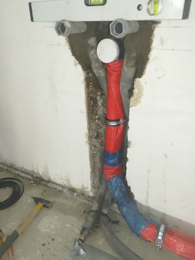 Laid water pipes behind a wall opening: red (hot), blue (cold) with clamps.