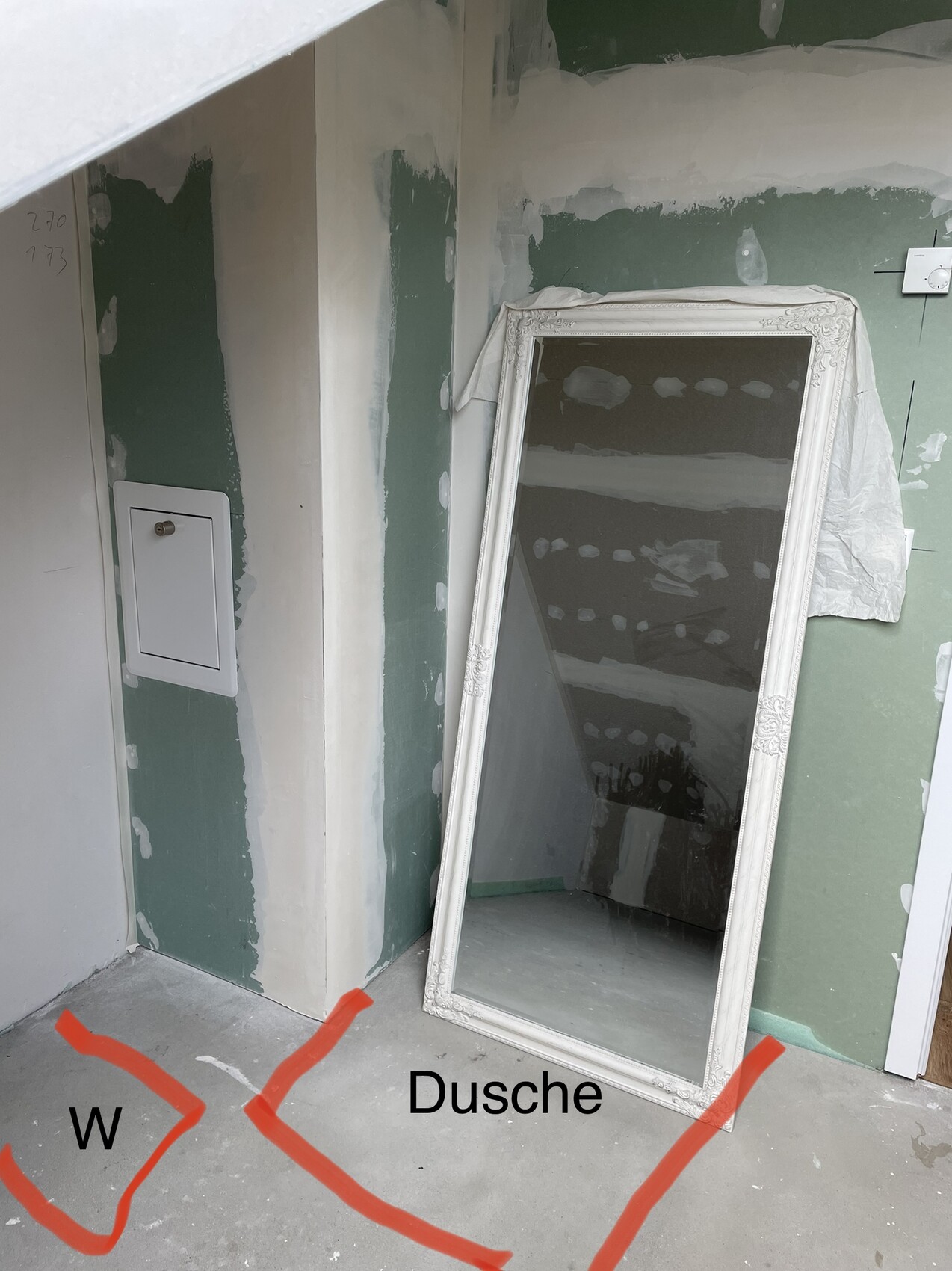 Large ornate mirror leaning against green painted wall in renovated bathroom next to shower