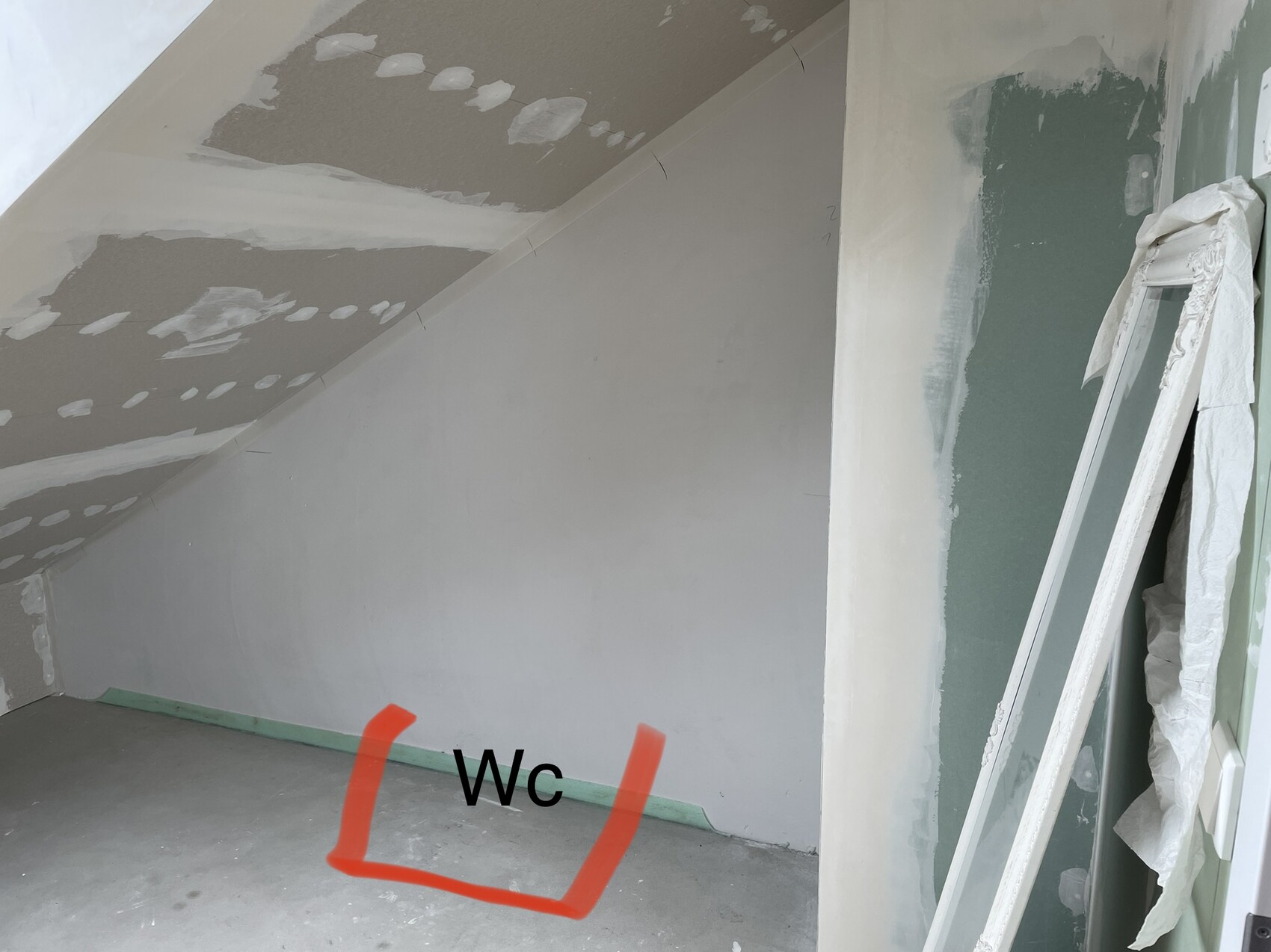 Unfinished attic room with sloped ceiling; floor marked for toilet area.