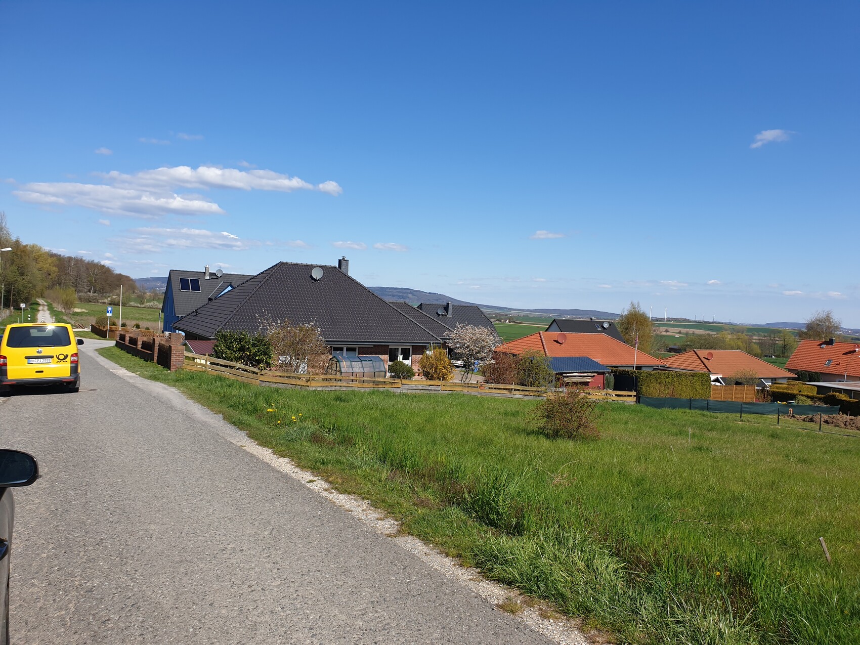 Suburban street with yellow delivery van on the left, terraced houses with roofs, and green field.