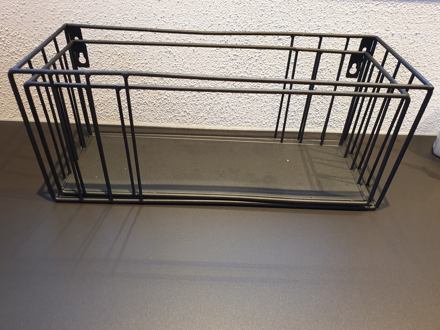 Black rectangular metal wire basket as an open storage container on the floor.