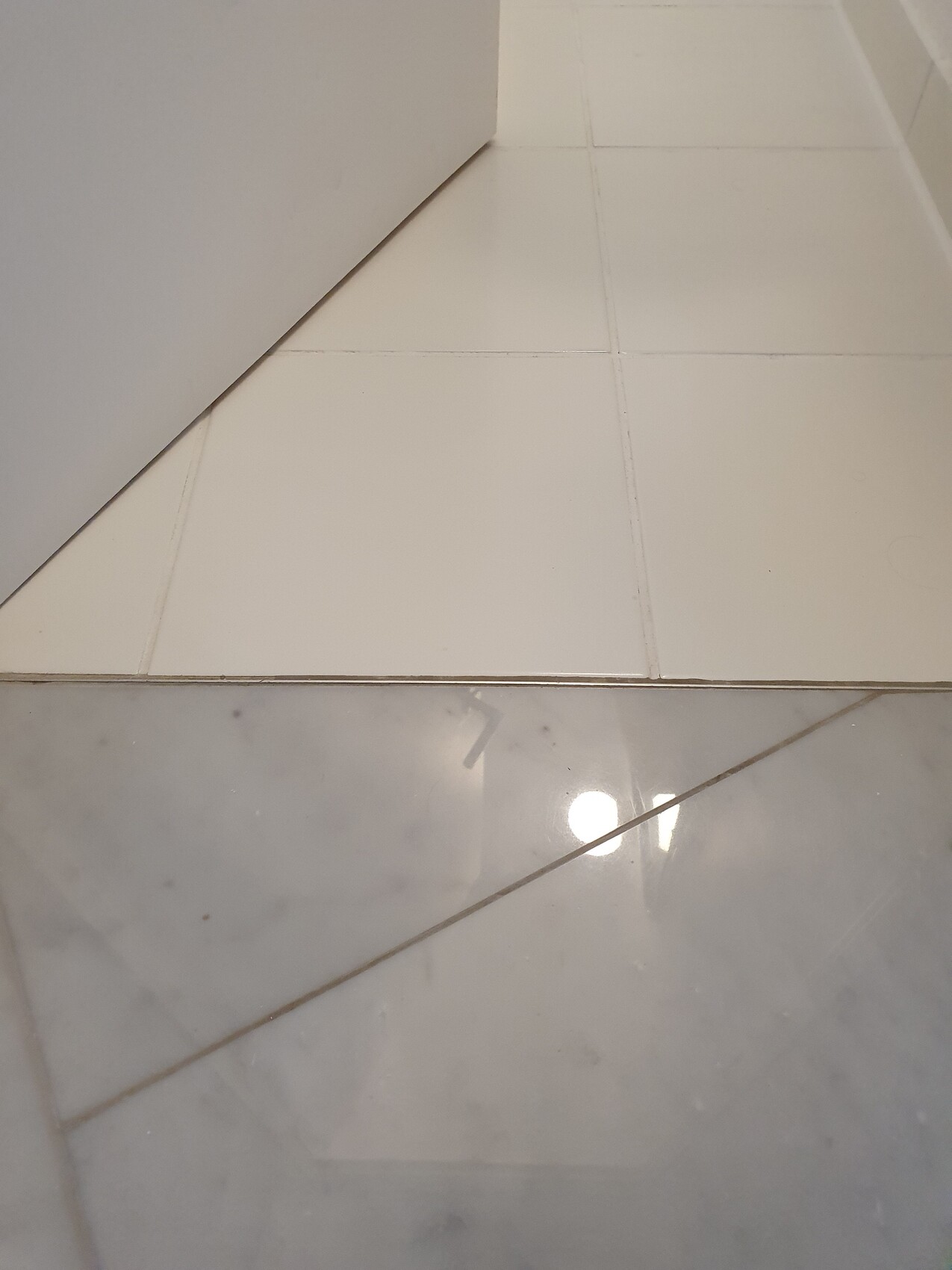 Floor area with light tiles; underneath grey marble tiles, transition strip, left wall edge visible.