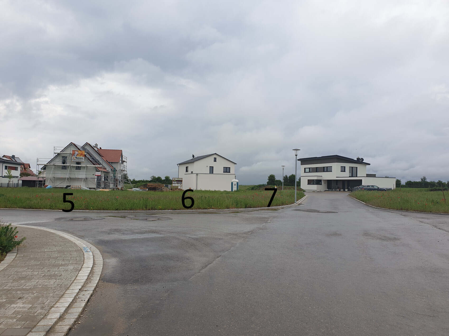 Building plot with a scaffolded house on the left and a modern house on the right under cloudy sky