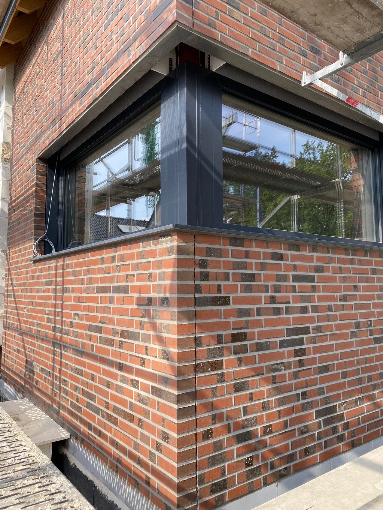 Corner house made of red bricks with large window in dark metal frame; scaffolding in the background.