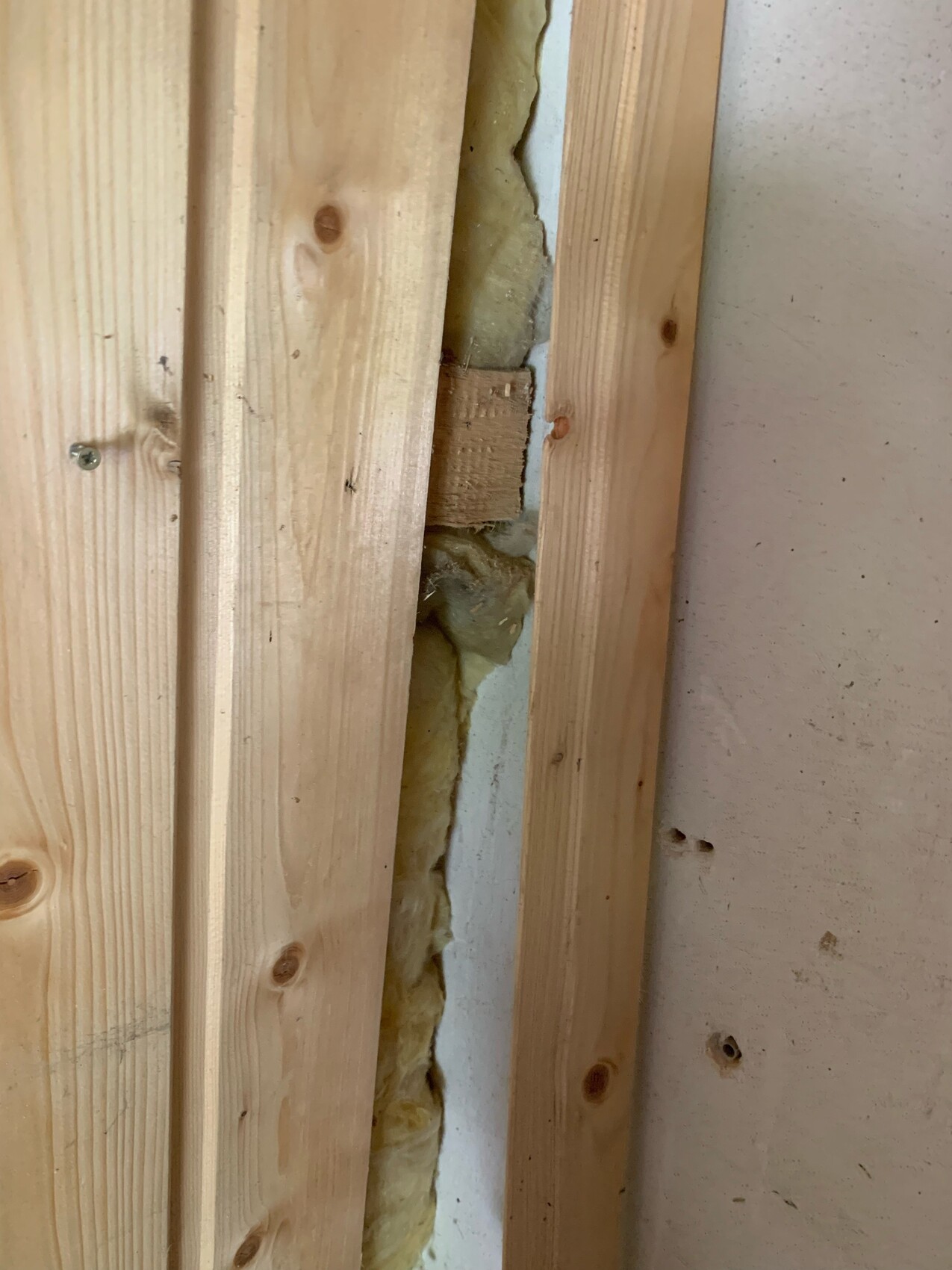 Unverputzte Wand mit Holzständerwerk, gelber Dämmstoff zwischen den Latten sichtbar.