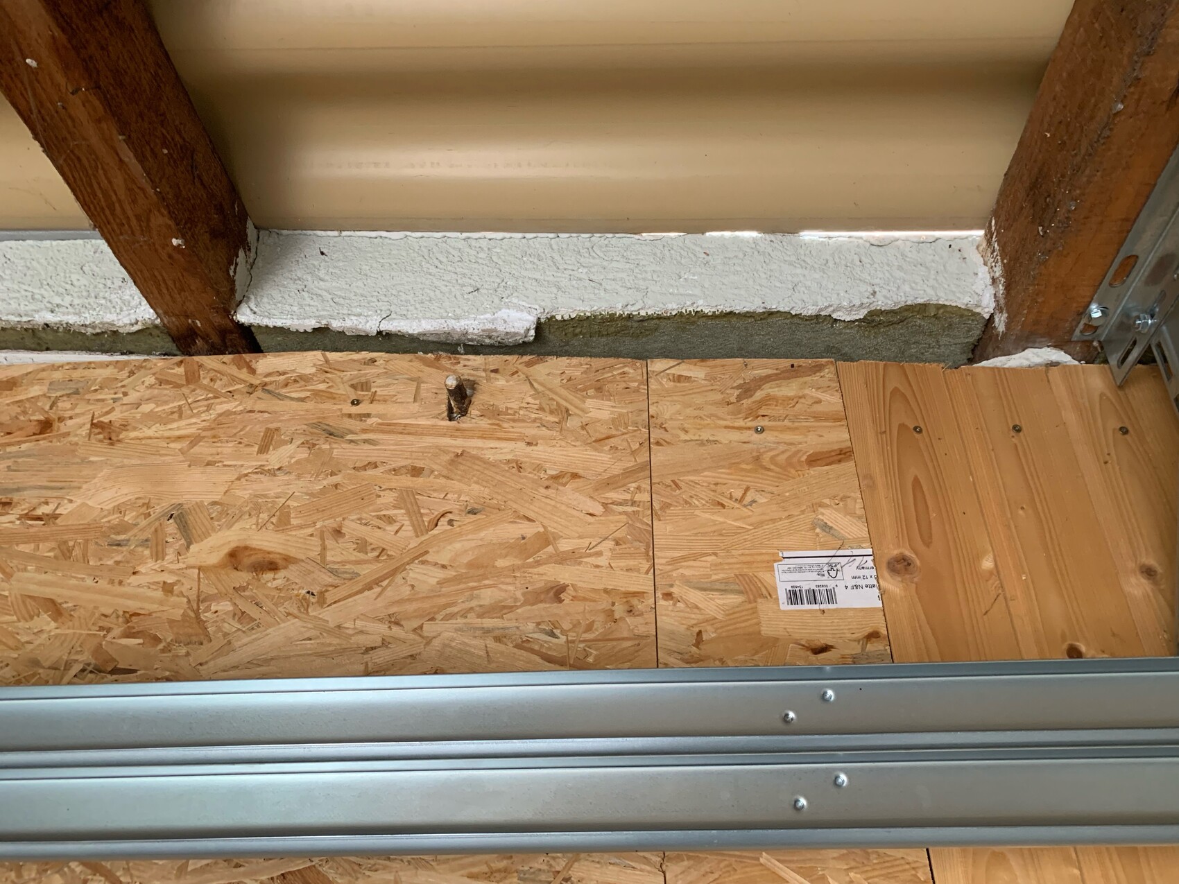 Baustellenboden mit OSB-Platten, Holzbalken, weißer Wandkante und Metall-Schiene am Boden.