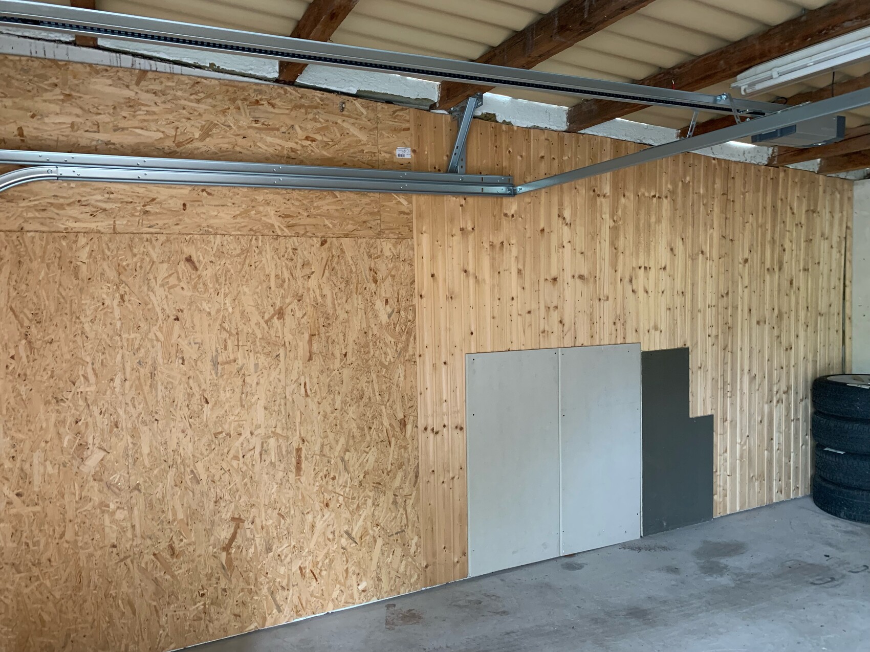 Garage/Werkstatt: OSB-Wand links, Holzpanelen rechts, Deckenstrukturen, Reifenstapel rechts.
