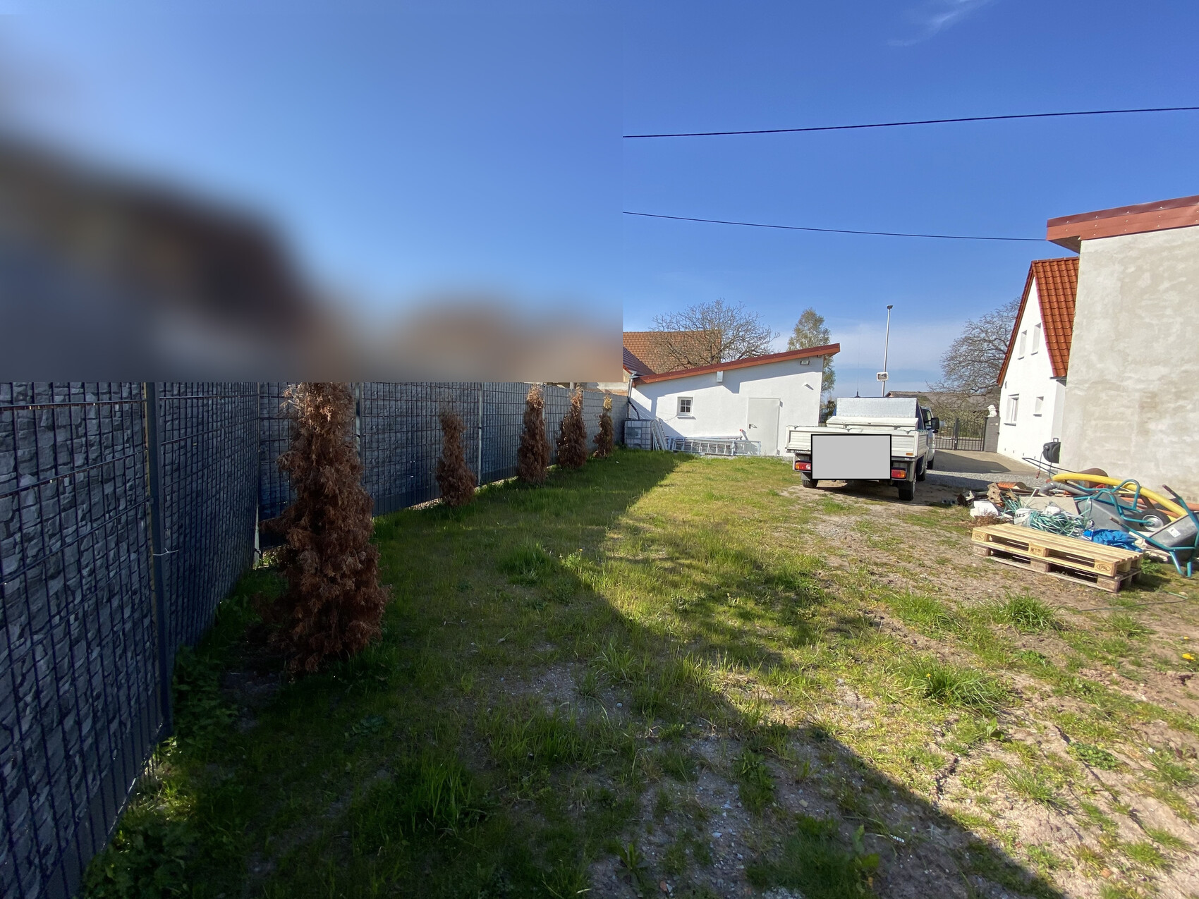 Garden/yard with grass, left fence, brown dead shrubs, white houses, pickup delivery van, pallets.