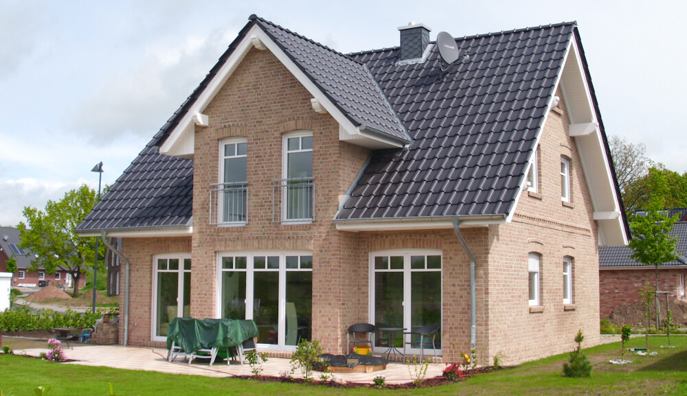 Two-story brick house with a dark tiled roof, large windows, and a terrace in the garden.