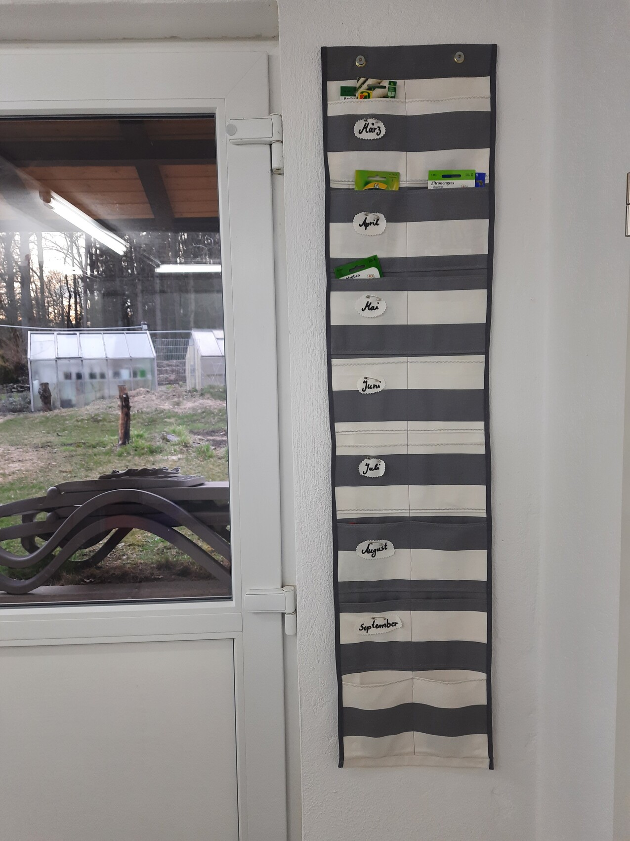 Slim, striped monthly organizer with compartments March–September on the wall next to the door.