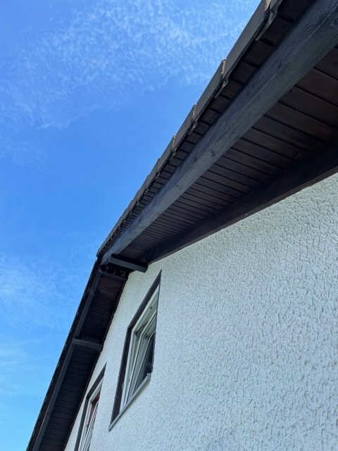 Lower roof overhang of a white plastered house, looking up at window and blue sky
