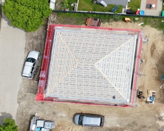 Aerial view of a house with visible wooden roof structure, red covering, construction site