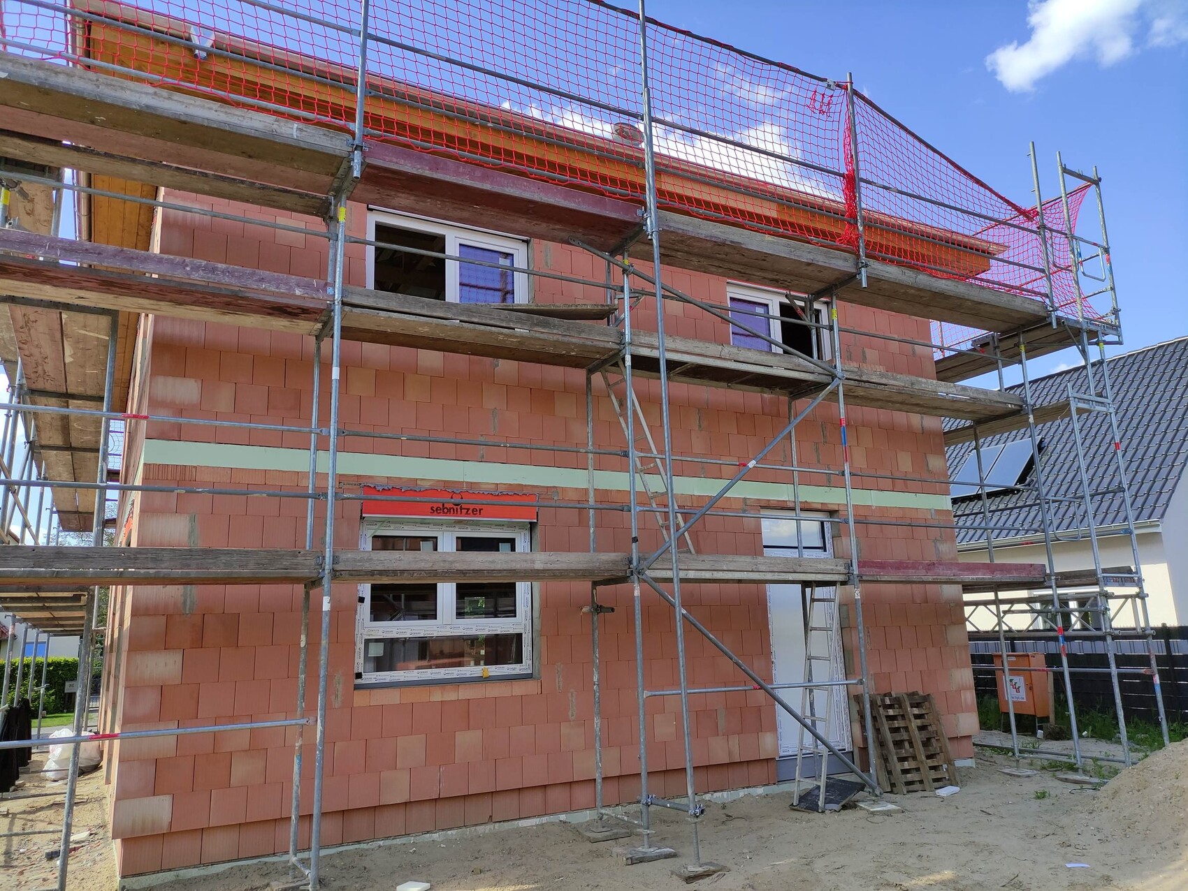 Newly built house with scaffolding, red safety nets, orange-brown brick walls, and open windows.