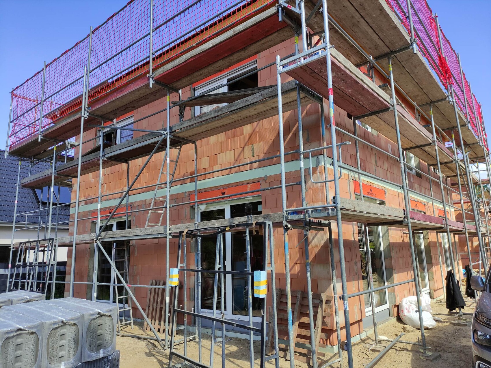 House construction: scaffolding around reddish-brown brick walls, pink fall protection.