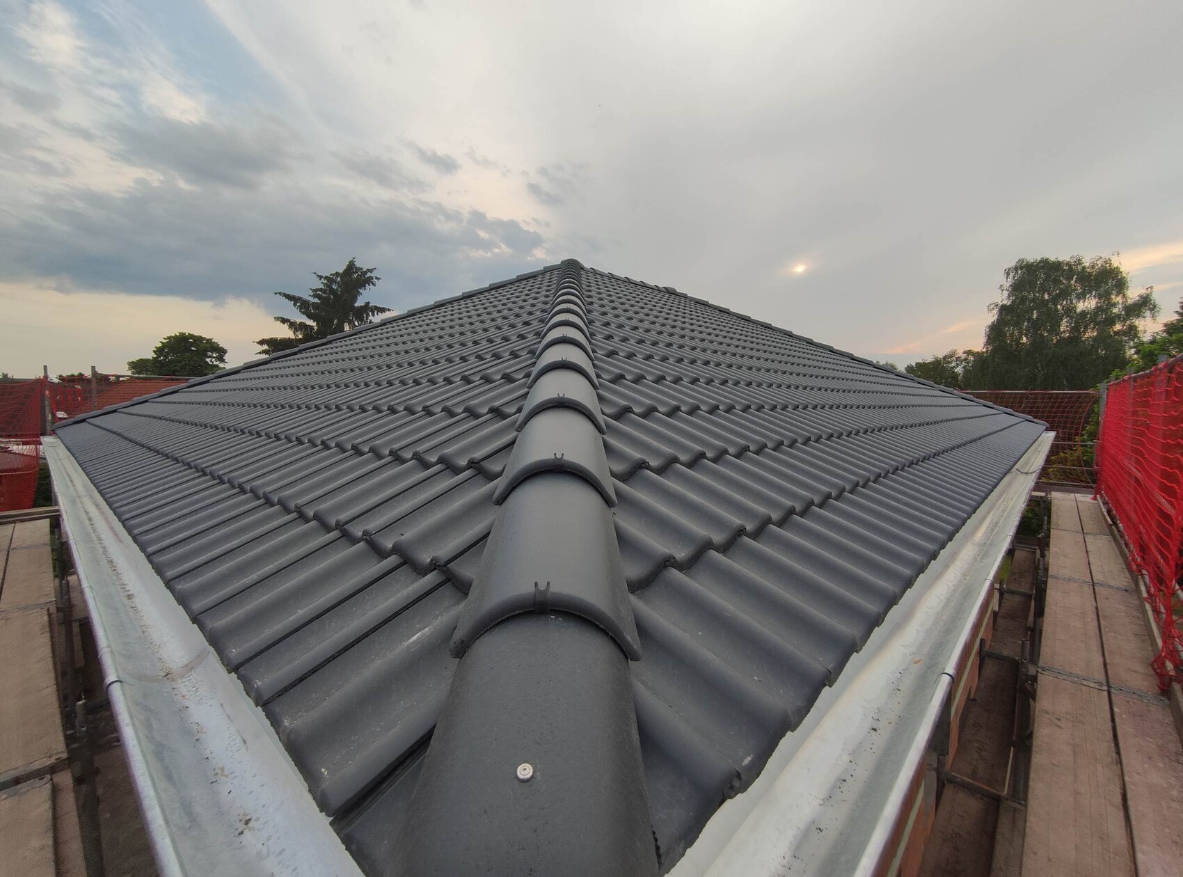 Top view of dark, wavy tiled roof with central ridge; construction scaffolding on sides.