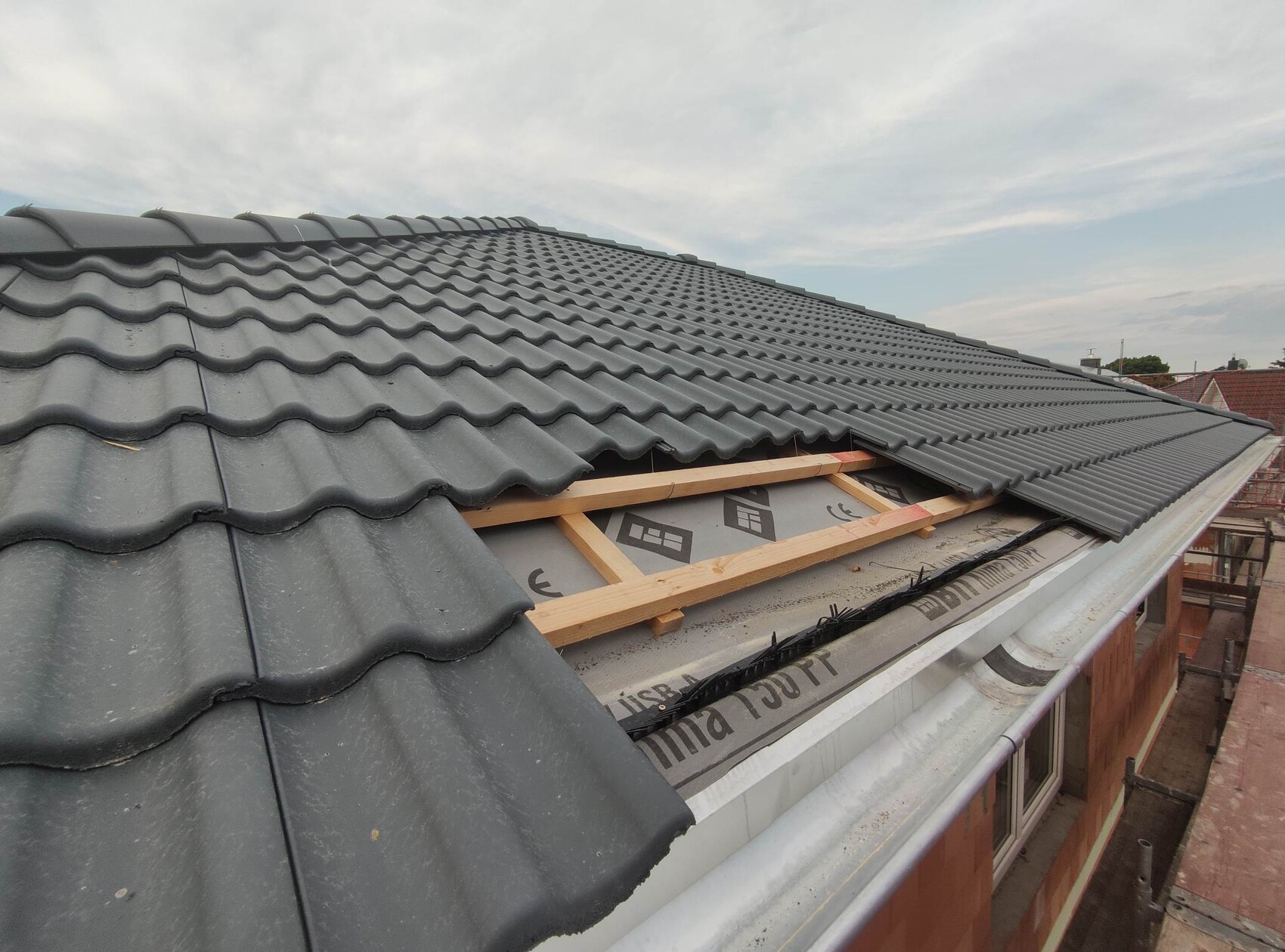 Roof with gray wavy tiles; open roof area with wooden frame, construction underlayment visible.