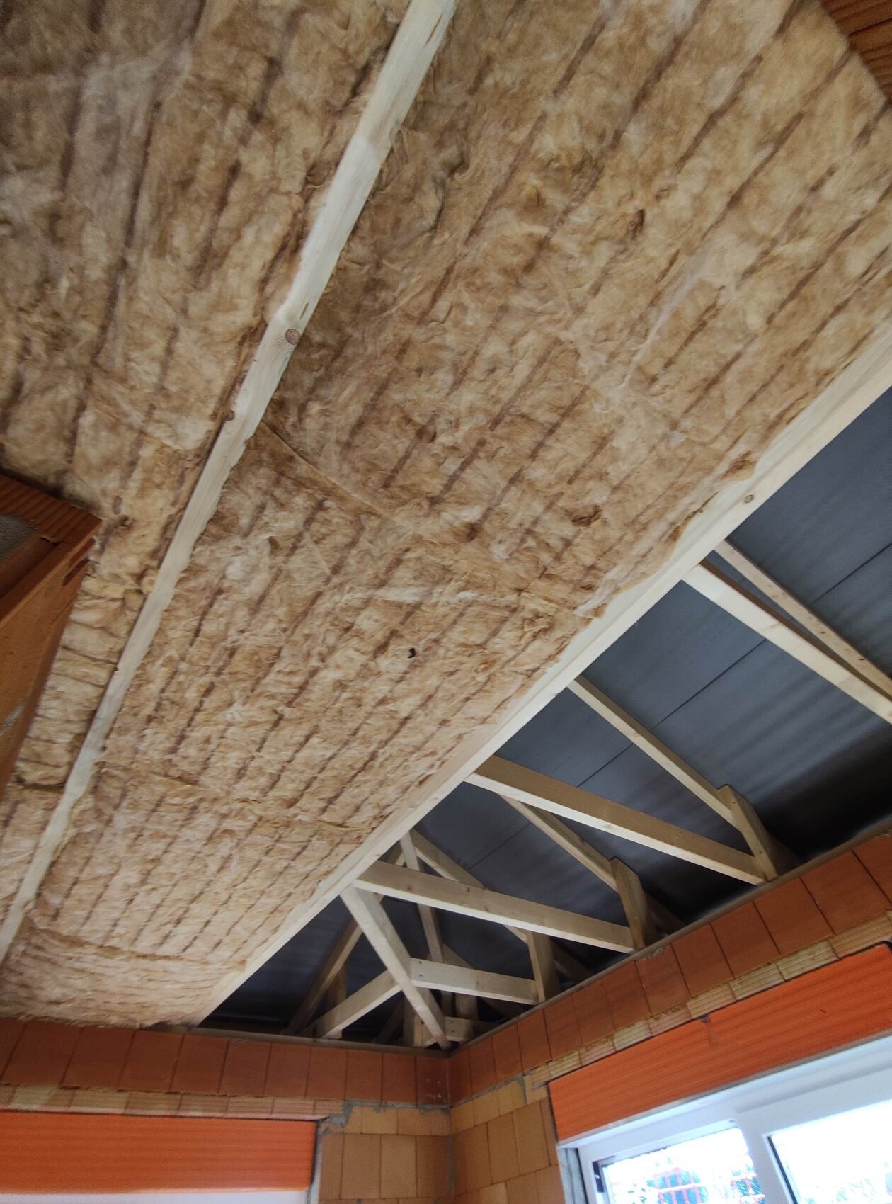 Attic interior view: mineral wool insulation between wooden rafters, visible roof structure.