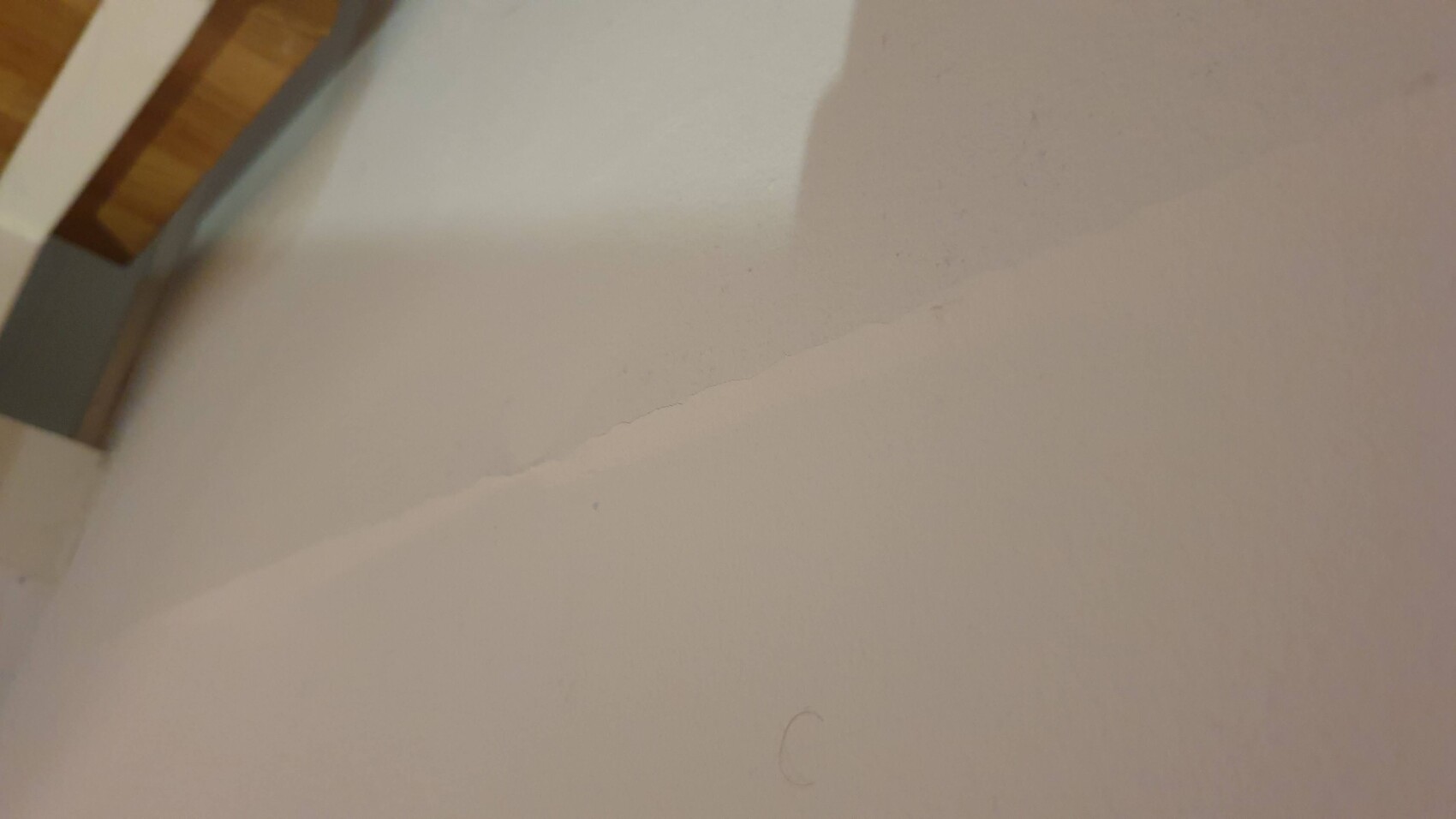 Weiße Wand mit diagonal verlaufender Kante, links Holzrahmen, Schatten darüber.