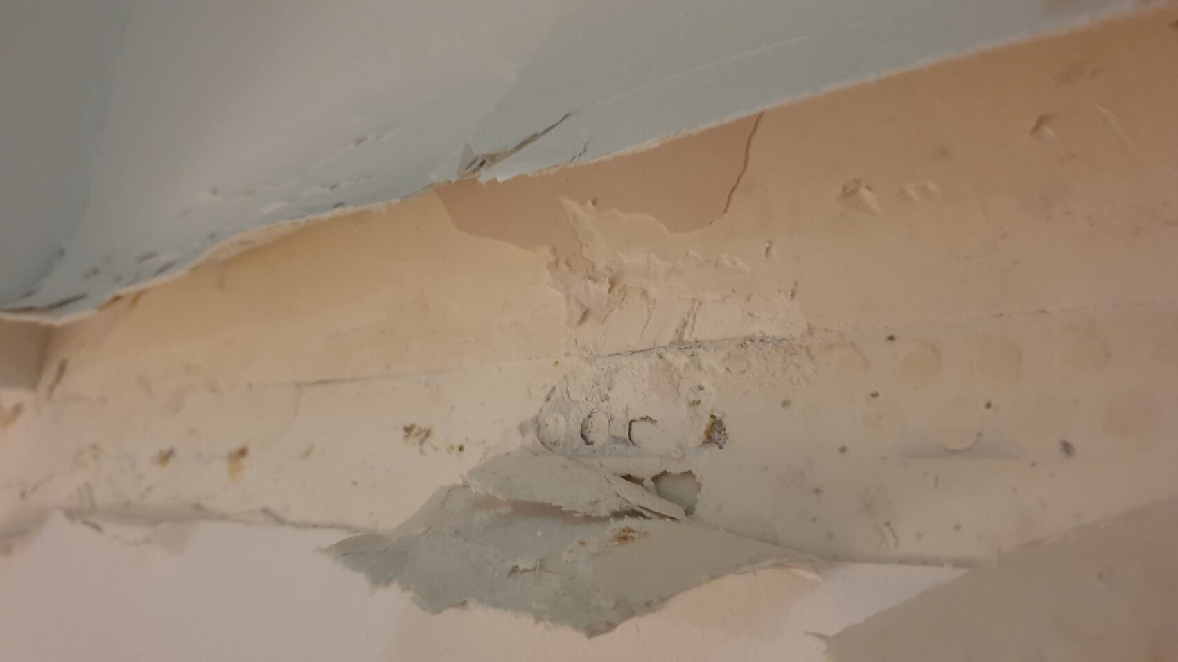 Nahaufnahme einer beschädigten Putzwand mit abblätterndem Putz und Rissen.