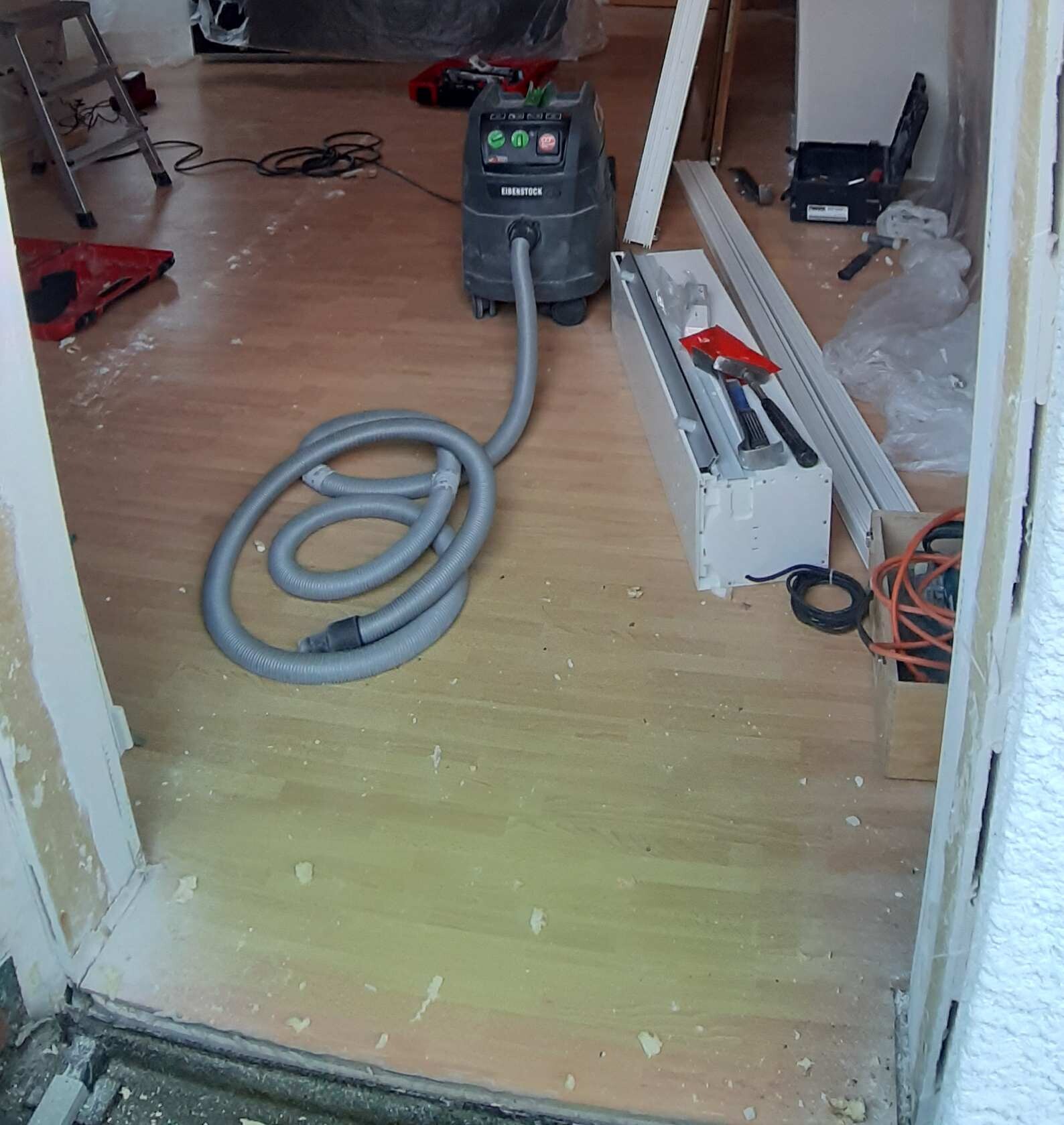 Renovierungsarbeiten in einem Zimmer: Staubsauger mit Schlauch und Bauwerkzeuge auf dem Boden.