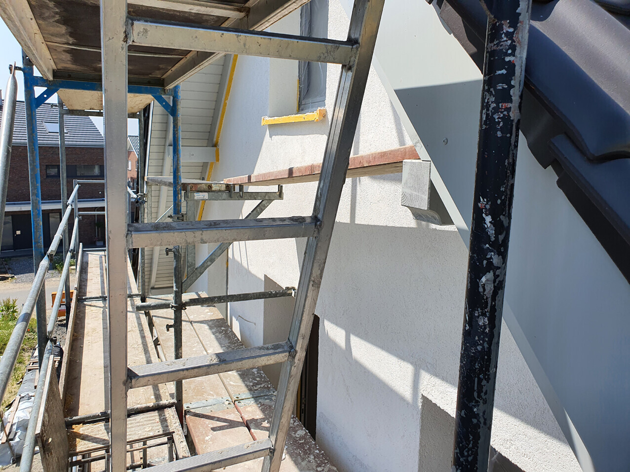 Construction scaffolding made of metal in front of a white building facade; view along the ladders.