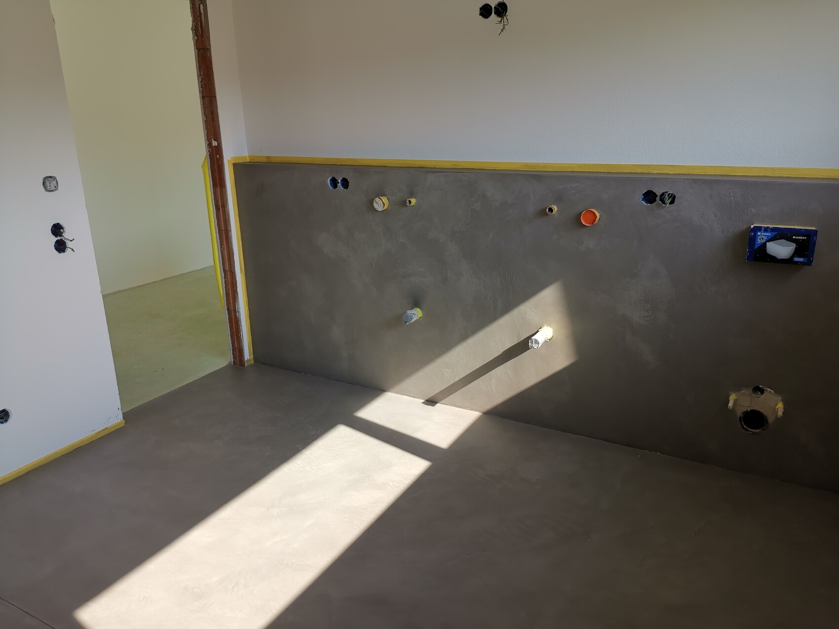Unfertige Innenwand in Küche/Bad mit Rohranschlüssen, Steckdosenlöchern und gelbem Abklebeband.