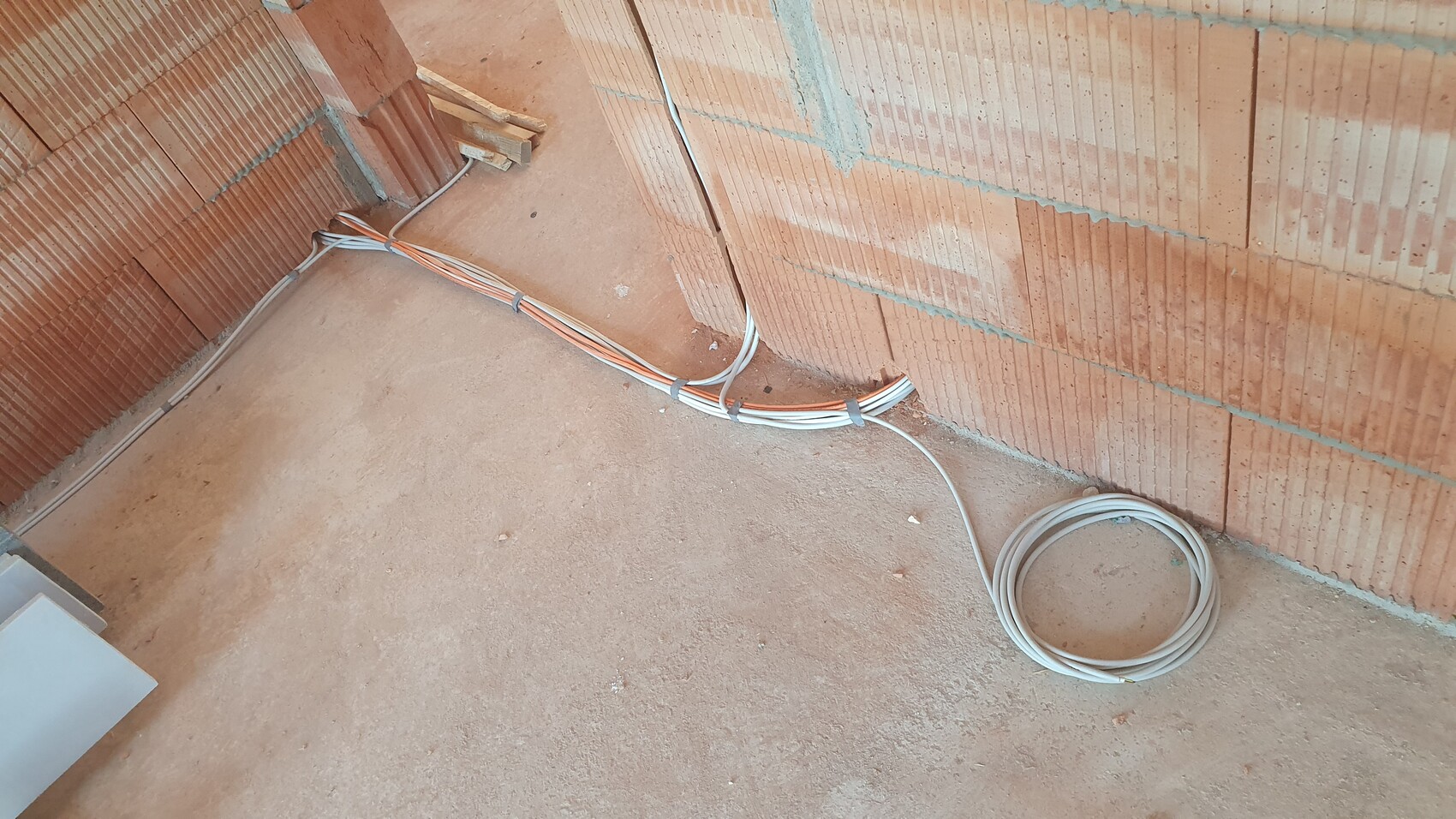 Construction site with exposed brick walls; cable bundles lying on the floor along the wall.