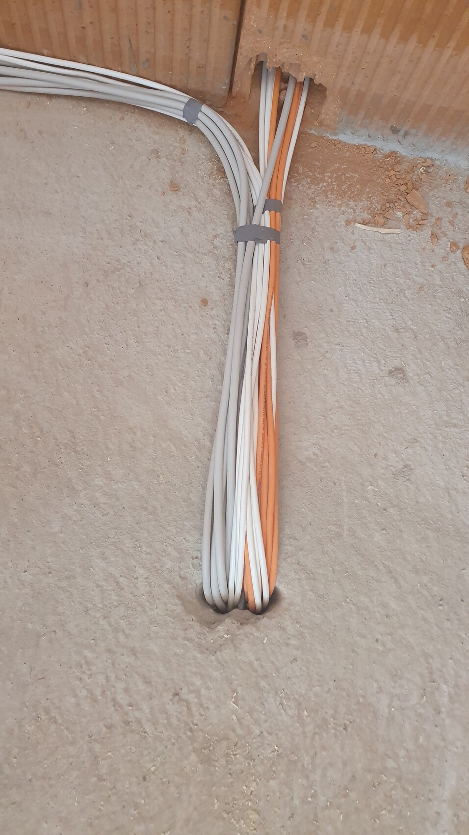 Cable bundles of white and orange wires passed through a hole in the wall, tied together.