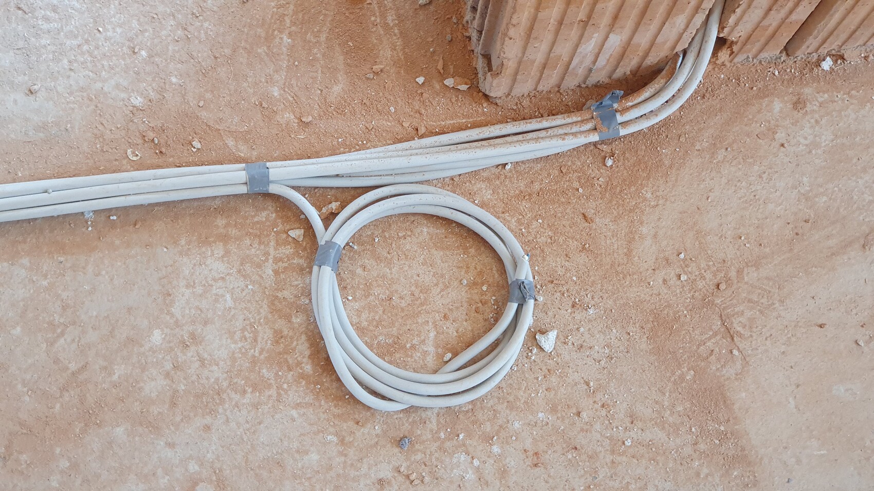 White electrical cables lying on dusty construction ground, tied in loops, a cable corner visible.
