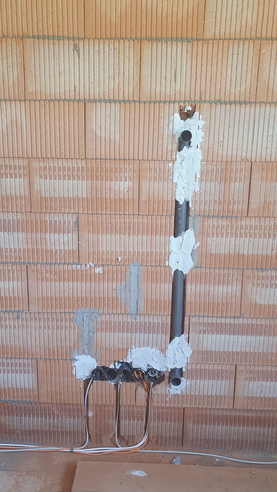 Plastered brick wall with vertical conduit and multiple cable penetrations with cables at the bottom.