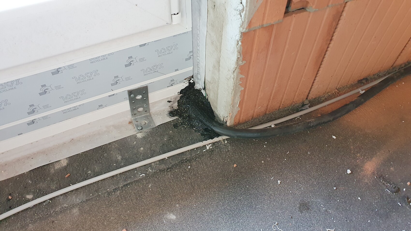 Exterior view: door frame, black sealant around cable at the foundation of a brick wall.